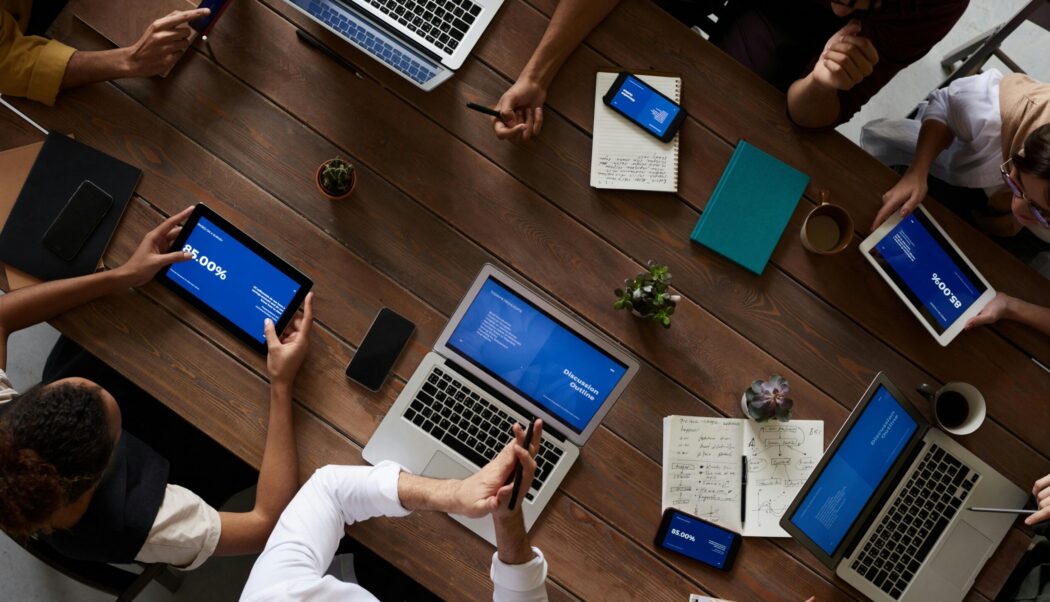 Plusieurs personnes de l'équipe d'AccessiWeb discutent autour d'une table de réunion. La photo est prise par dessus la tabler ne permettant pas de voir le visage des employés et/ou clients.